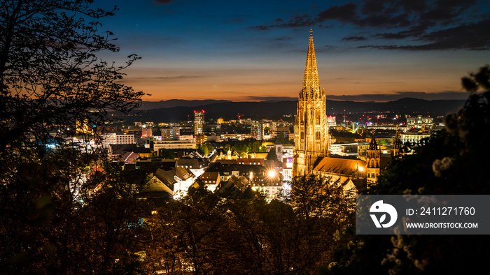 Germany, Freiburg im Breisgau, Magical orange sunset sky above skyline of the beautiful city and muenster by night in blue hour atmosphere