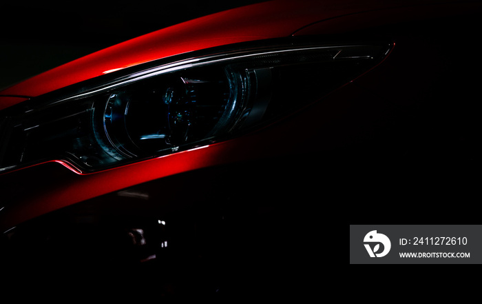 Closeup headlight of shiny red luxury SUV compact car. Elegant electric car technology and business concept. Hybrid auto and automotive concept. Car parked in showroom or motor show. Car dealership.