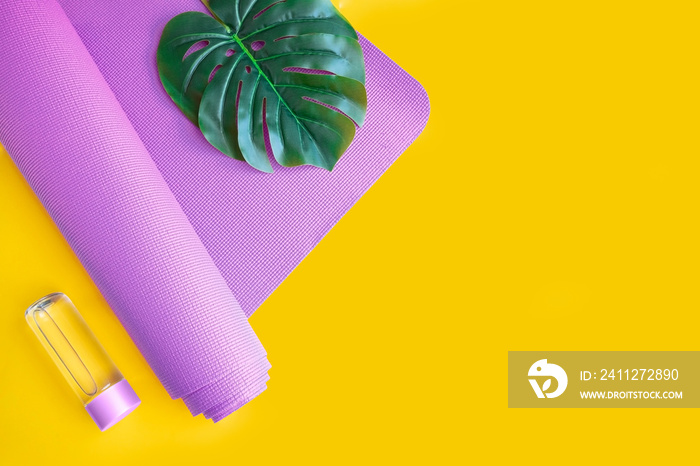 Close up of lilac exercise mat and water bottle on yellow background with palm leaf. Concept for practice yoga, pilates or any  physical workout  at summer.