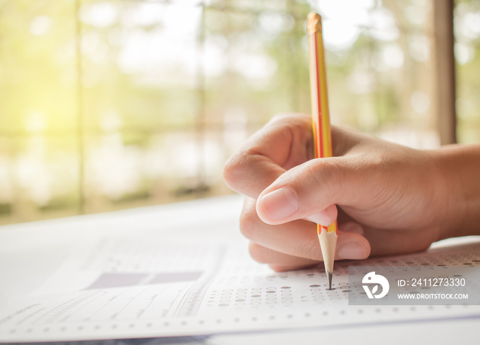 hand student testing in exercise and taking fill in exam carbon paper computer sheet with pencil at school test room, education concept