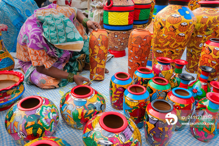 Female Indian artist painting colorful terracotta pots, works of handicraft, for sale during Handicraft Fair in Kolkata.