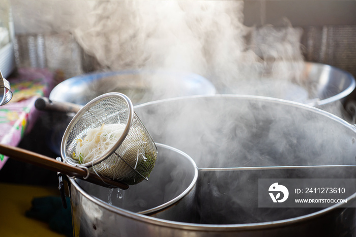 Hand of Thai Chef with Noodles in a basket that just boiled from hot soup pot with steam soup to ramen,  Chef or cooker will put the soup that has been boiled into ingredients such , junk food concept