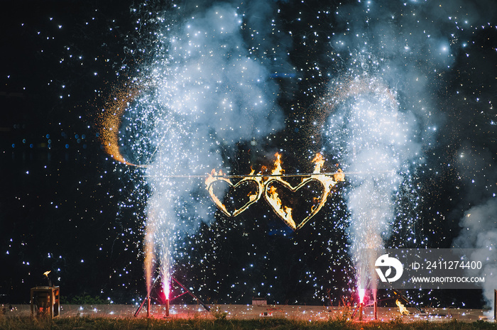 A burning fiery heart, sparks, decorations from an outdoor fire show. Beautiful and bright fireworks in nature on a festive day at a wedding. Gift for newlyweds.