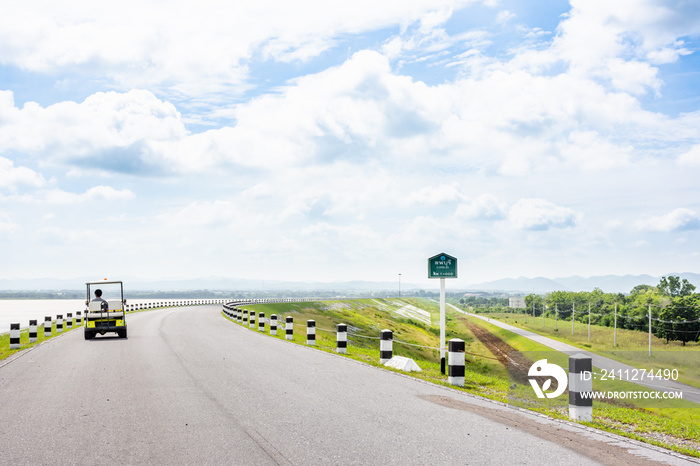 Landscape Scenic road travel on empty highway and  Electric Golf Cart near a large reservoir with sky and clouds background.Pa Sak Jolasid Dam Thailand.