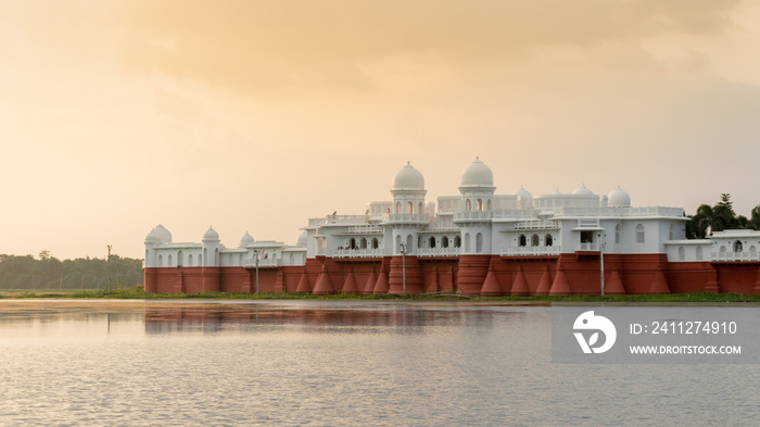 Evening sunset view of the lake place with red and white walls, beautiful domes and archways amid calm and serene water, Tripura, India