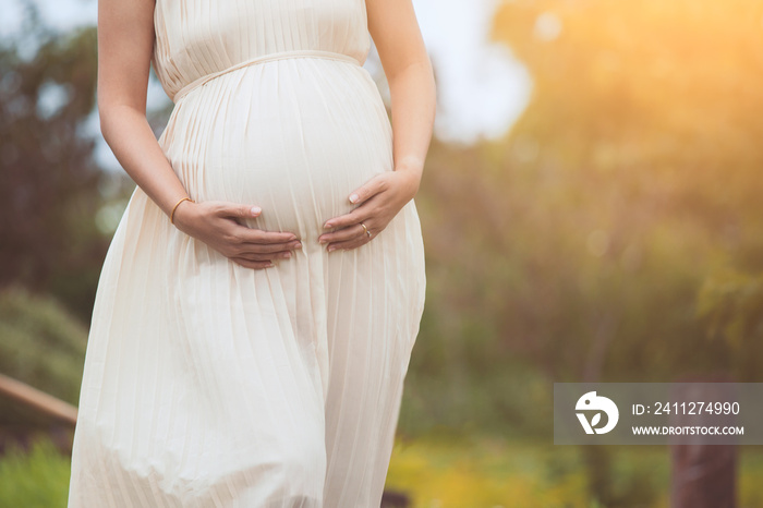 Pregnant woman touching her big belly and walking in the park relaxing in outside