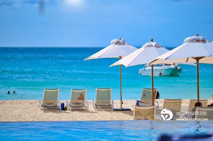 White sand beach and blue sea landscape view of a tropical resort hotel beside modern swimming pool, white parasols, palm trees, deck beach chairs in the golden sunset time