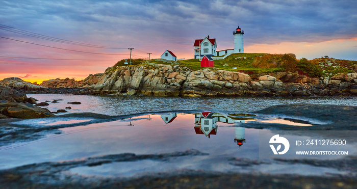 Maine lighthouse reflecting in puddle on rock during golden morning light with overcast clouds