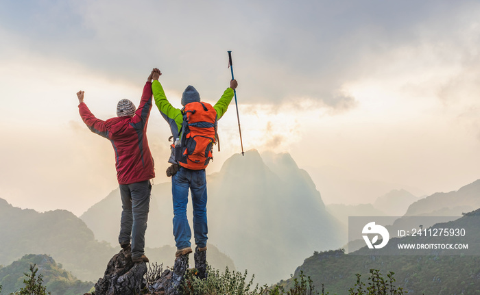 Successful two hiker standing with raised hands on top thailand mountain at the sunset time.