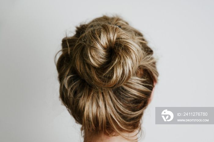 A view of the woman’s hair from the back. Fashion and hairdressing concept. The girl, turned back, shows her hair bunched up in a bun on a light background.