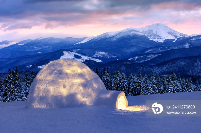 Real snow igloo house in the winter mountains. Snow-covered firs and mountain peaks on the background. Foggy forest with snowy spruce