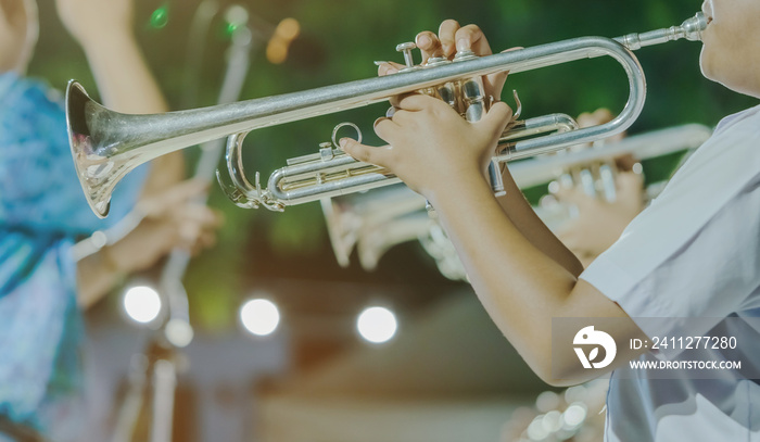 Male student with friends blow the trumpet with the band for performance on stage at night.