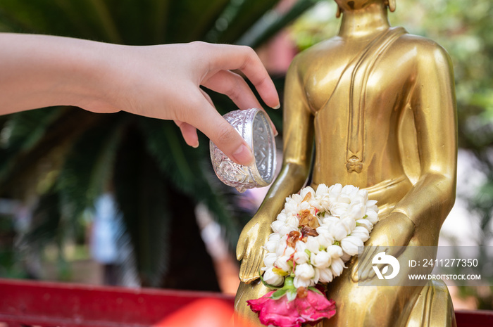 Close up of woman hand pouring down scented water to Buddha statue during the Songkran festival in Thailand. This water festival marks the beginning of the traditional Thai New Year.