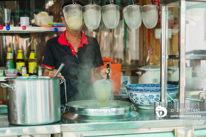 Man making noodles soup at noodle stall on street.