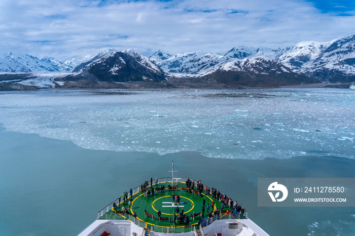 Cruise ship is sailing at the Hubbard Glacier. Many people on a helipad are watching huge iceberg