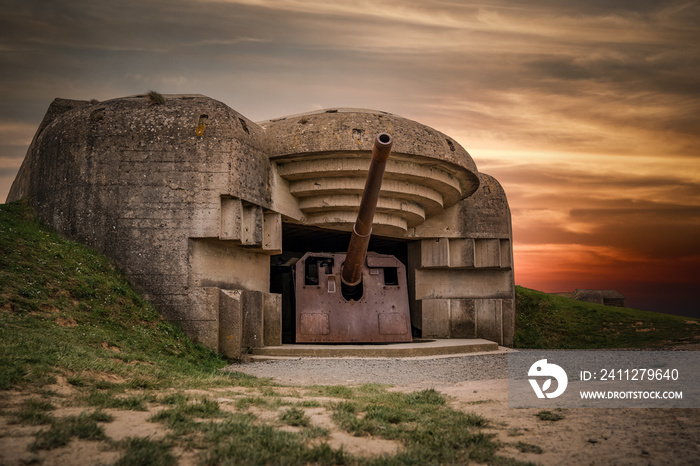 Atlantic wall concrete German World War Two gun emplacement fortification bunker battery at Longues-sur-mer in Normandy Gold Beach France remains lay in ruins with beautiful orange sunset sky