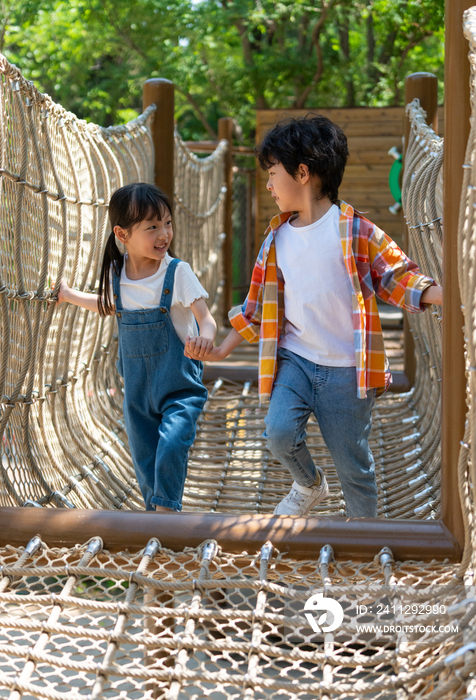 两个小孩子相互鼓励牵手走绳桥