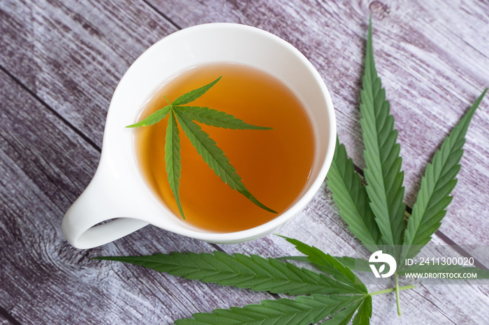 Marijuana herbal tea and cannabis leaves in a cup. Cup with cannabis tea and cannabis leaves on wooden background, copy space.