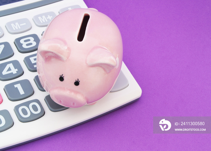 Piggy bank and calculator on purple background, save money concept