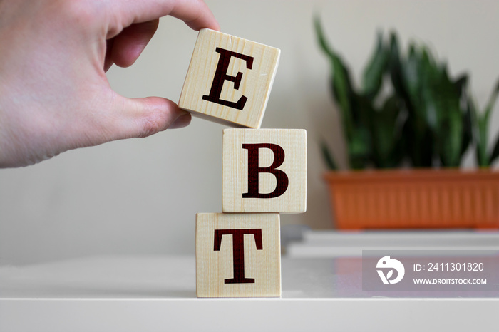 Hand holding wood cube block with ’EBT’ text. EBT - short for Earnings Before Interest and Taxes