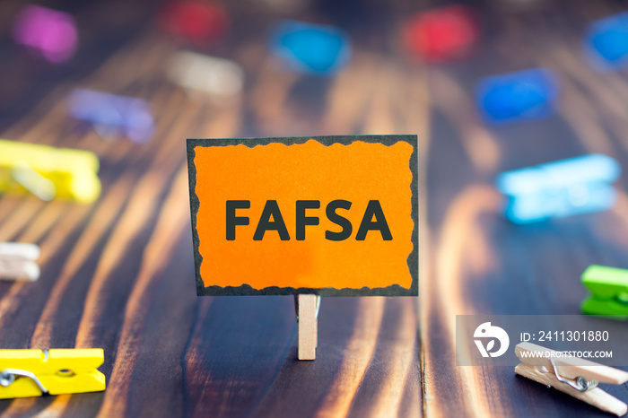 sign board with an inscription FAFSA, Free Application for Federal Student Aid, on a wooden background and colored clothespins