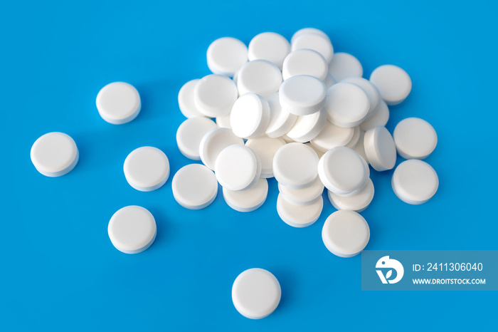 Pile of white pills on light blue background. Many disc shaped tablets. Chalky and not coated. No imprints. Drug abuse concept