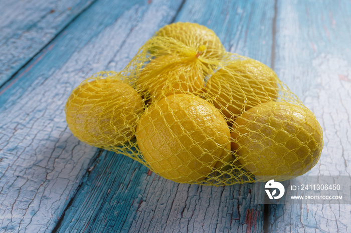 Close up of yellow lemons in a net package, on blue background.