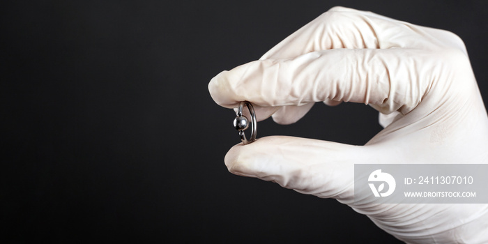 silver piercing ring , accessory for piercing in hand on a dark background.