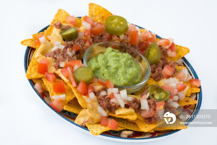 Mexican nachos with beef, guacamole, cheese sauce, peppers, tomato and onion in plate isolated on white background