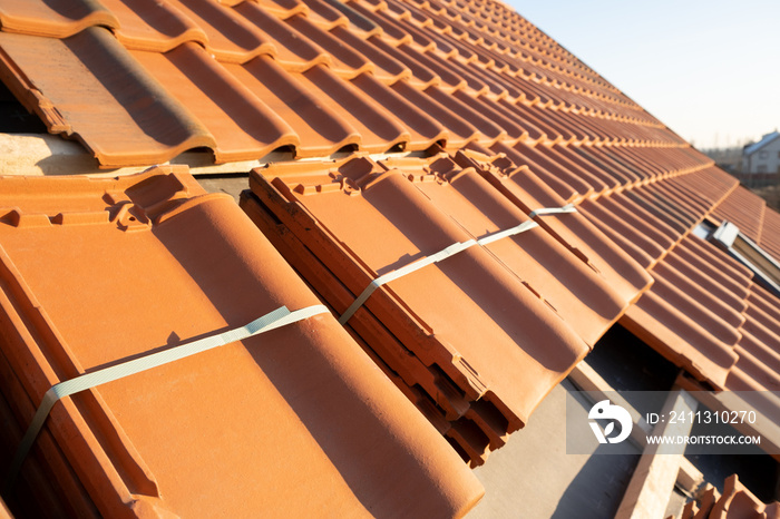 Stacks of yellow ceramic roofing tiles for covering residential building roof under construction.