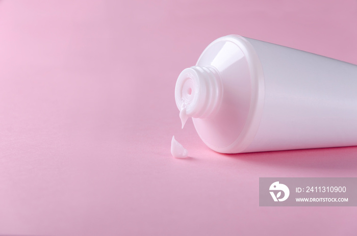 White tube with cream and squeezed drop of it on the pink background.Closeup of cosmetic product on the pink surface