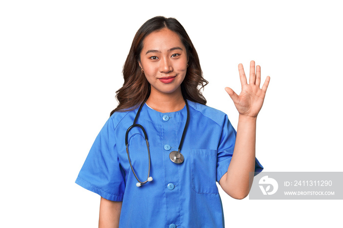 A young nurse chinese woman smiling cheerful showing number five with fingers.