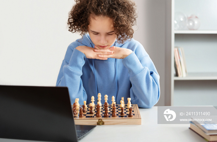 Female teenager play chess with himself. She ponder a move. Home hobby, learning to play chess with laptop from Internet.