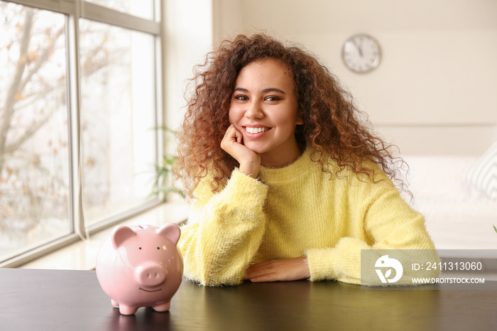 African-American woman with piggy bank at home