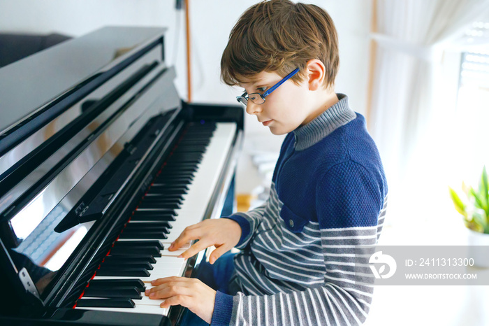 School boy with glasses playing piano in living room. Child having fun with learning to play music instrument. Talented kid during homeschooling corona virus lockdown.