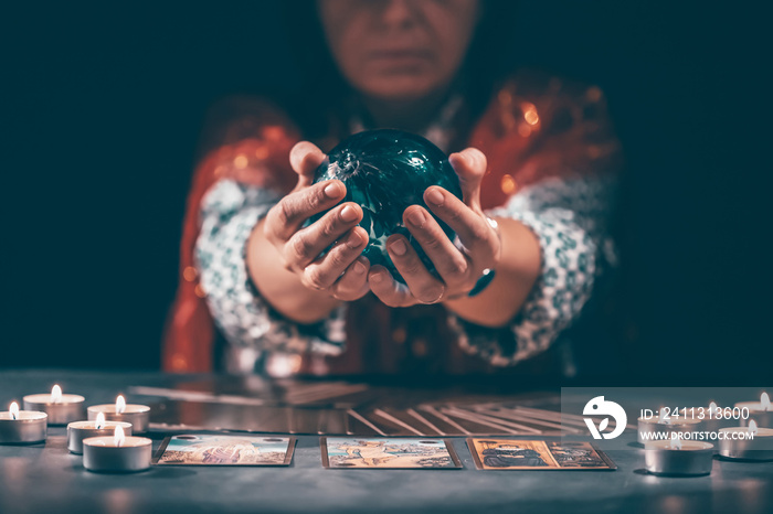 Tarot reader with tarot cards.Tarot cards face down on table near burning candles and crystal ball.