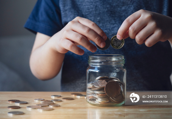 Cropped shot Kid hand putting money coins into clear jar,  Child counting his saved coins, Childhood hand holding coin, Children learning about saving for future concept