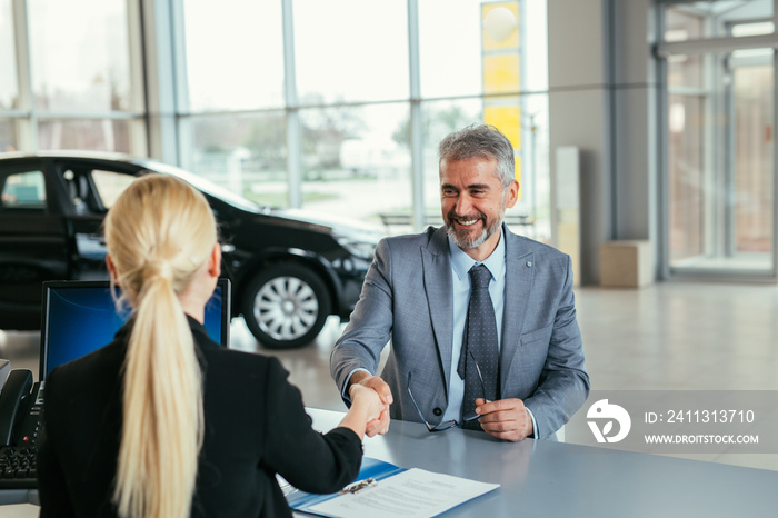 businessman shaking hands with sell agent in car showroom