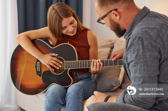 Private lesson. Guitar teacher showing how to play the instrument to young woman