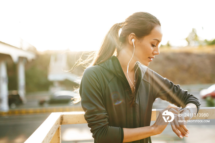 Image of young focused woman using earphones and smartwatch