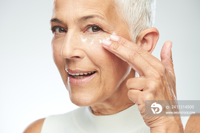 Gorgeous smiling Caucasian senior woman trying out new anti age cream. Beauty photography.