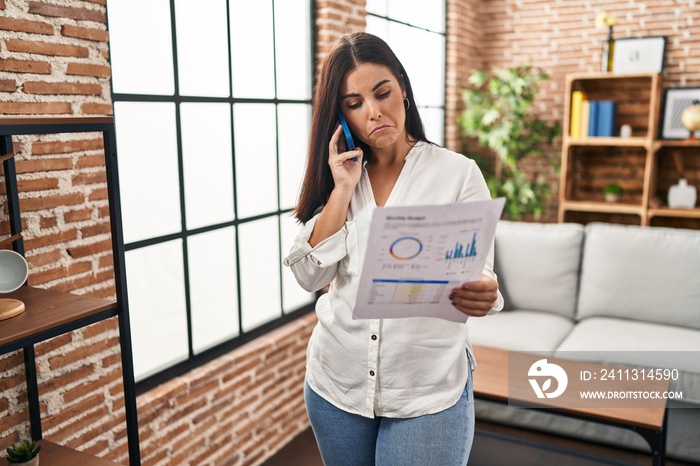 Young hispanic woman speaking on the phone about bills depressed and worry for distress, crying angry and afraid. sad expression.