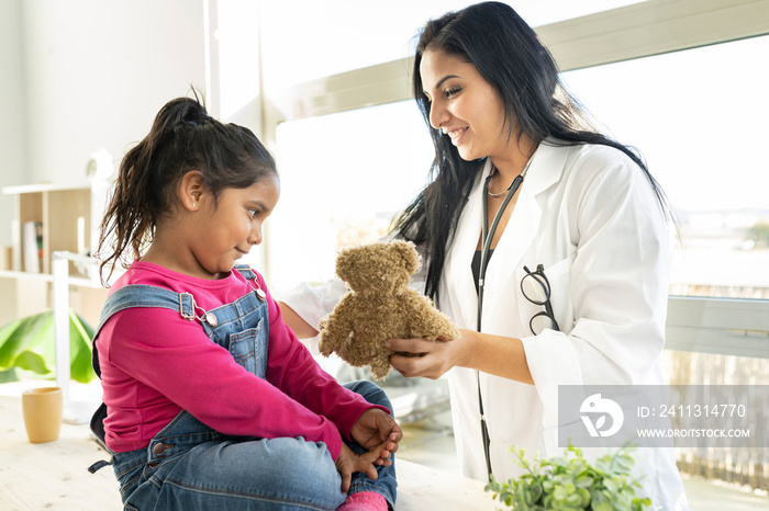 female doctor gives teddy bear to children