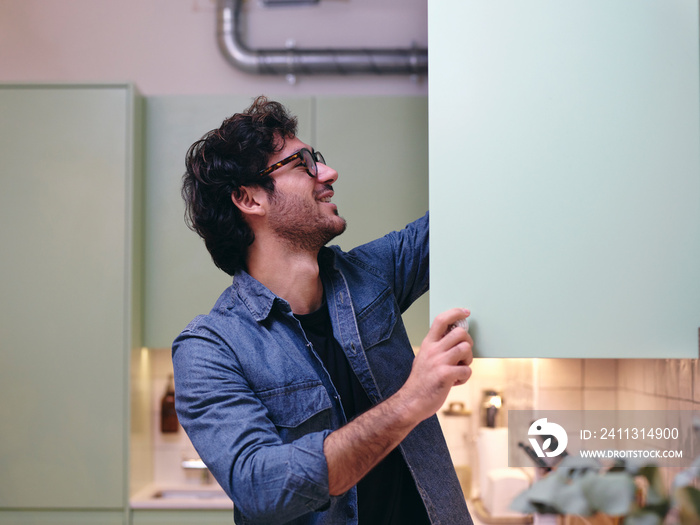 UK, London, Smiling man at open cupboard in kitchen