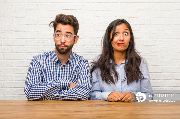 Young indian woman and caucasian man couple doubting and confused, thinking of an idea or worried about something