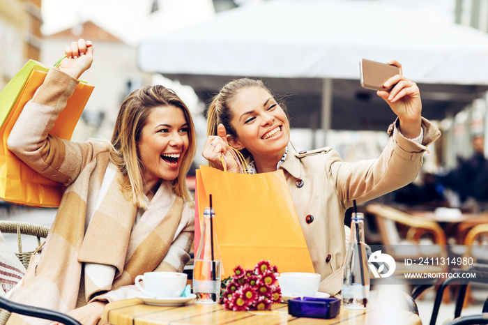 Two women friends taking a selfie in cafe after shopping