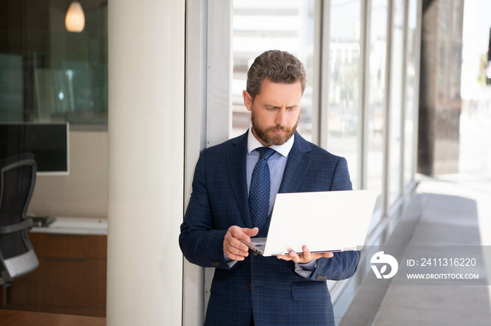 serious bearded mature man freelancer in suit chatting on laptop at business office, online chat