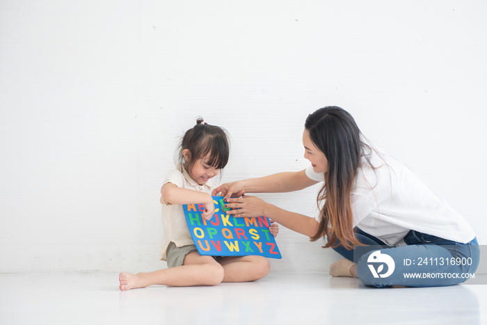 Young Asian mother taught her little daughter about reading English characters, having fun together, family concept
