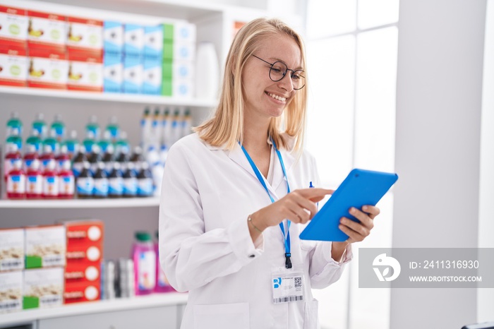 Young blonde woman pharmacist using touchpad working at pharmacy