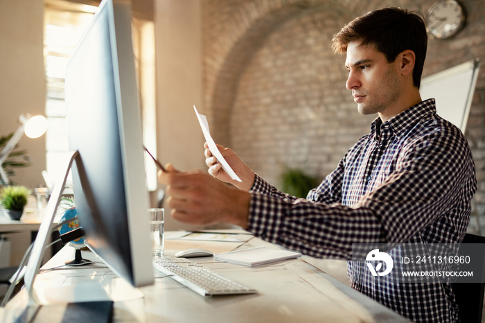 Young businessman using computer while analyzing reports in the office.